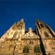Dóm v Regensburgu - na obrázku jeho západný portál - bol zriadený na mieste vyhorenej románskej baziliky z 11.storočia. Stavebné dejiny Dómu siahajú od r. 1250 až po pozastavenie stavieb v r. 1515; v 19.storočí vznikli zakončenia veží a barokové prístavby z obdobia okolo r. 1697, ktoré boli neskôr prinavrátené do gotického štýlu.
