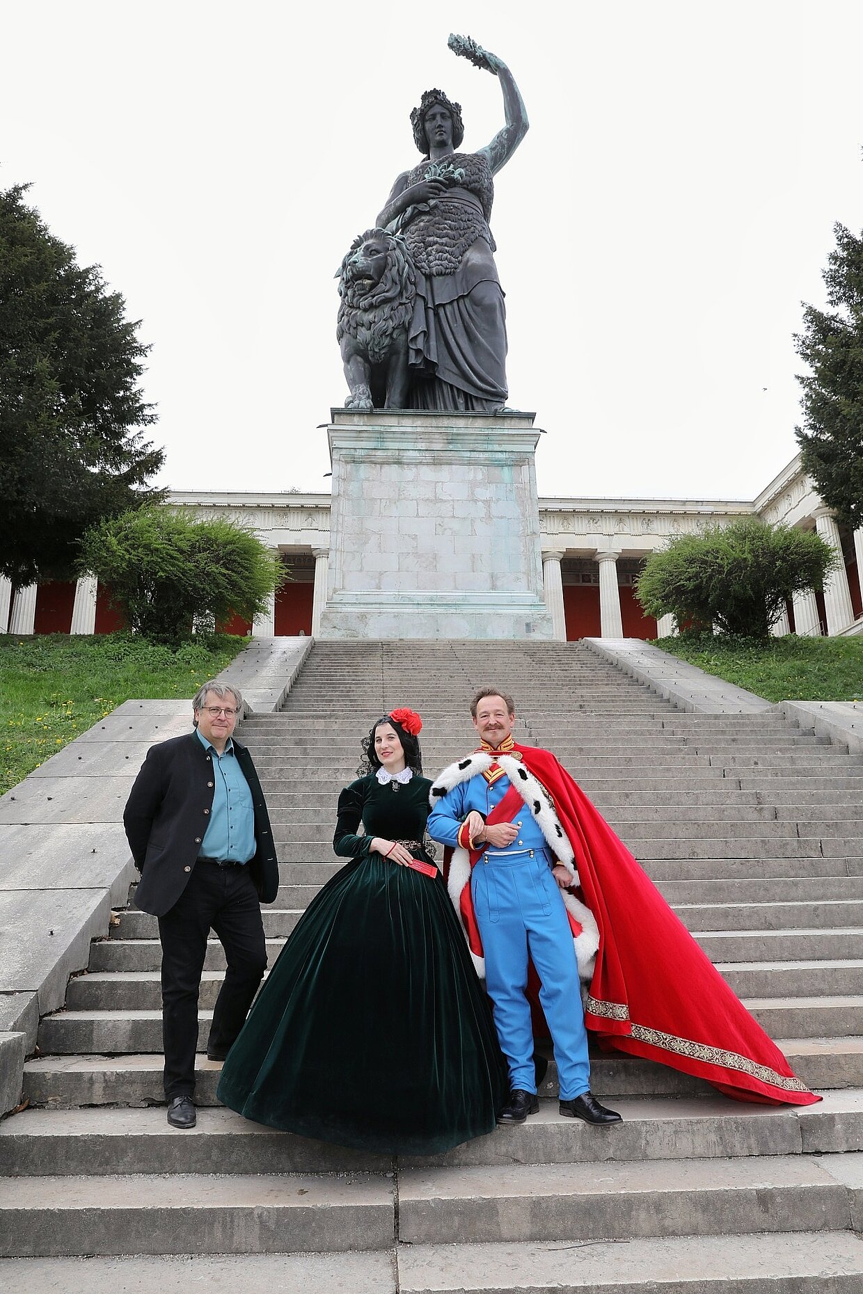 (v.l.n.r.) Dr. Richard Loibl, Direktor des Hauses der Bayerischen Geschichte mit Lola Montez dargestellt von Anna Günther und Holger Matthias Wilhelm als König Ludwig I. an der Bavaria am 16. April 2025. © Haus der Bayerischen Geschichte | Foto: Stefan Effenhauser