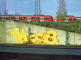 Von Spitzweg bis Graffiti. Die Eisenbahn als Motiv in der Kunst umfasst nahezu alle Genres – von der realistischen Darstellung einer revolutionären Technik bis zur allegorisch-symbolhaften Überhöhung als Metapher für die Unaufhaltsamkeit der Zeit, für Vergänglichkeit und Tod. Die zeitgenössische Graffitikunst wiederum nutzt Eisenbahn und Bahnhofsgelände als „Malgrundlage“ – ohne das Eisenbahnwesen scheint der Siegeszug der Graffitikunst kaum denkbar. Links ein seit einiger Zeit auf einer Mauer kurz vor dem Münchner Hauptbahnhof befindliches Piece; HCCB steht wohl für “High Capacity Color Barcode” – ein Strichcode von Microsoft. Und wohl vom selben Sprayer stammt das nicht weit entfernt an der gegenüberliegenden Seite der Bahnstrecke befindliche „Logo“ der bayerischen Daily-soap „Dahoam ist dahoam“ – ein liebevoll verziertes Lebkuchenherz. / Judith Bauer, München